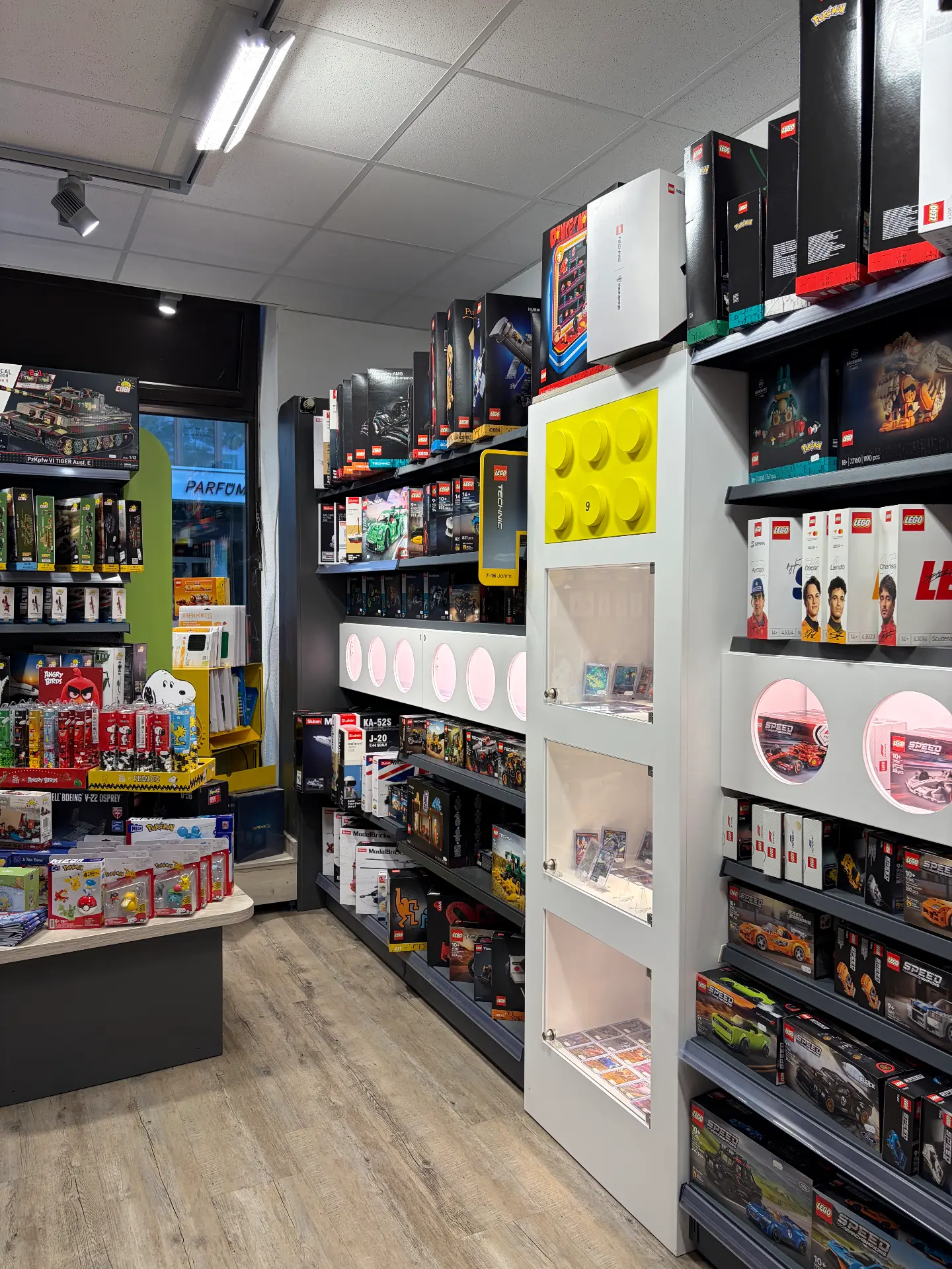 Regale mit LEGO Technic und Speed Champions, daneben Pokémon-Produkte und ein Vitrinenschrank
