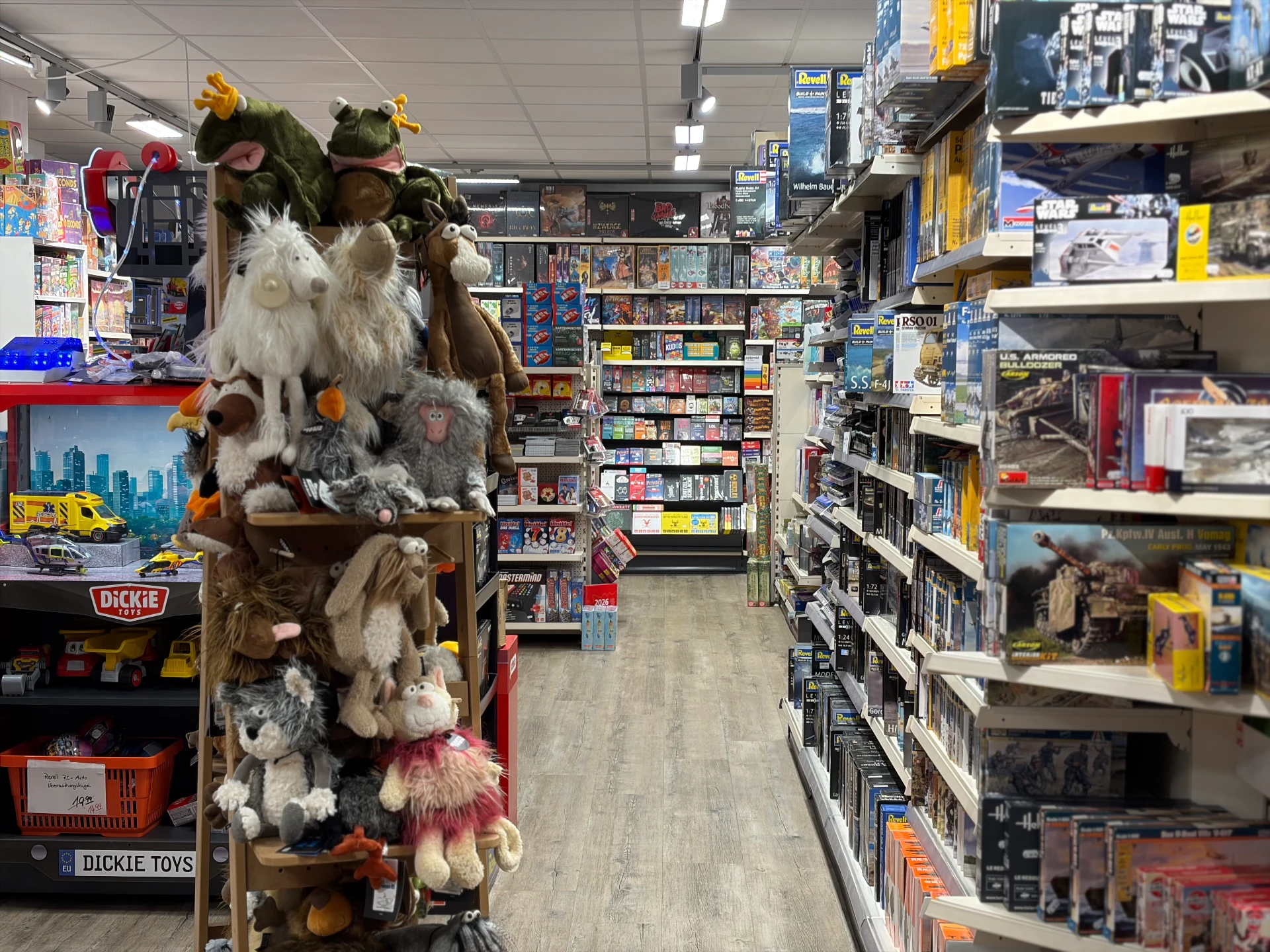 Gang mit einem Holzregal voller Plüschtiere und einem langen Regal mit Modellbausätzen