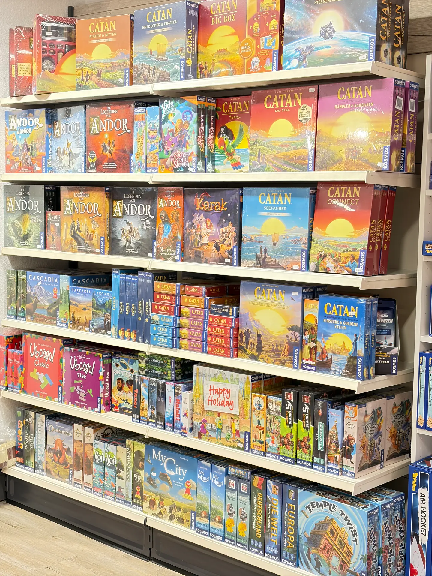 Hohes Regal voller Brettspiele, darunter Catan, Karak, Cascadia und Ubongo