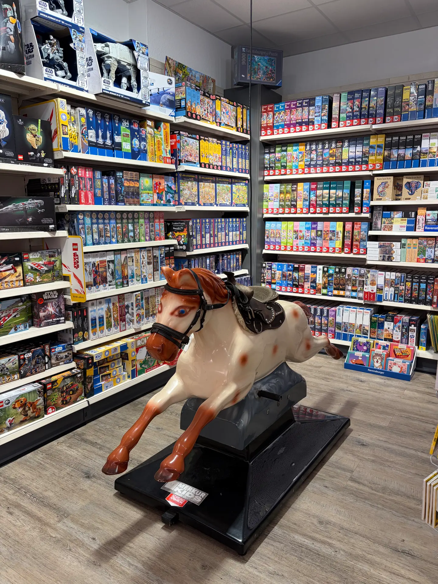 Weißes Schaukelpferd vor wandhohen Regalen voller Ravensburger-Puzzles und Star-Wars-Figuren